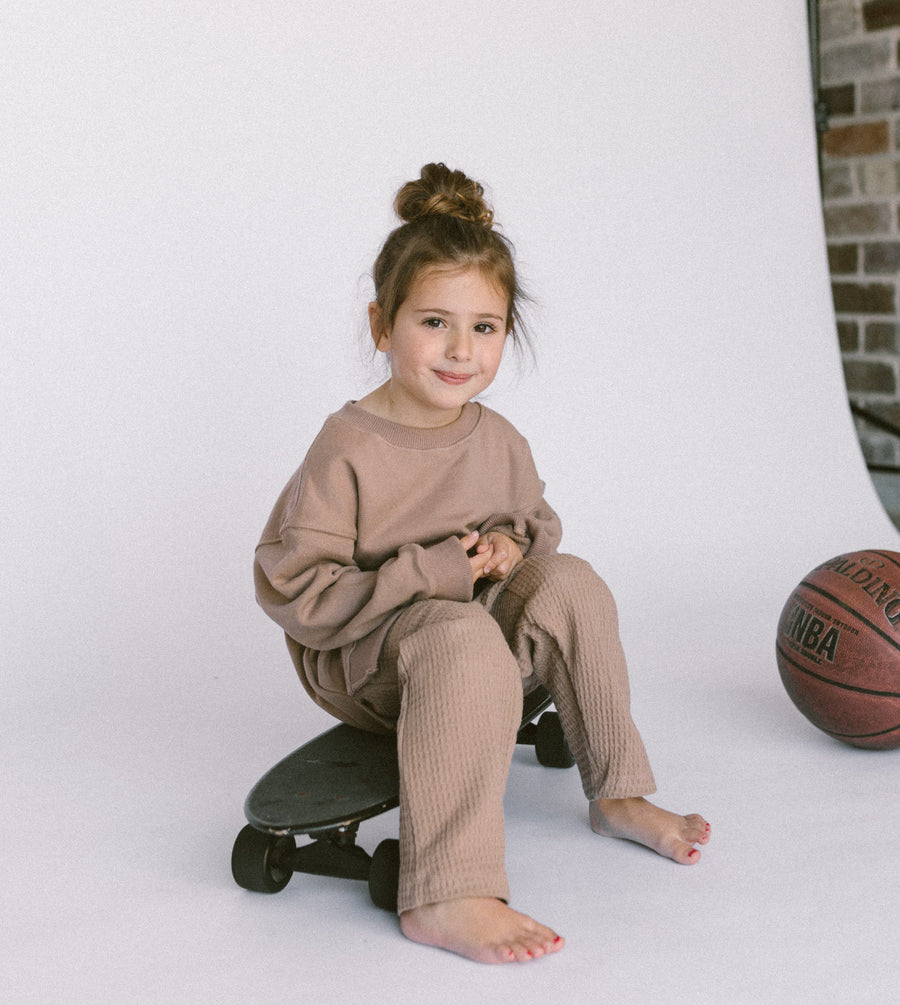 Girl sitting on a black skateboard wearing a waffle sweater set in brown by Zaja the Label