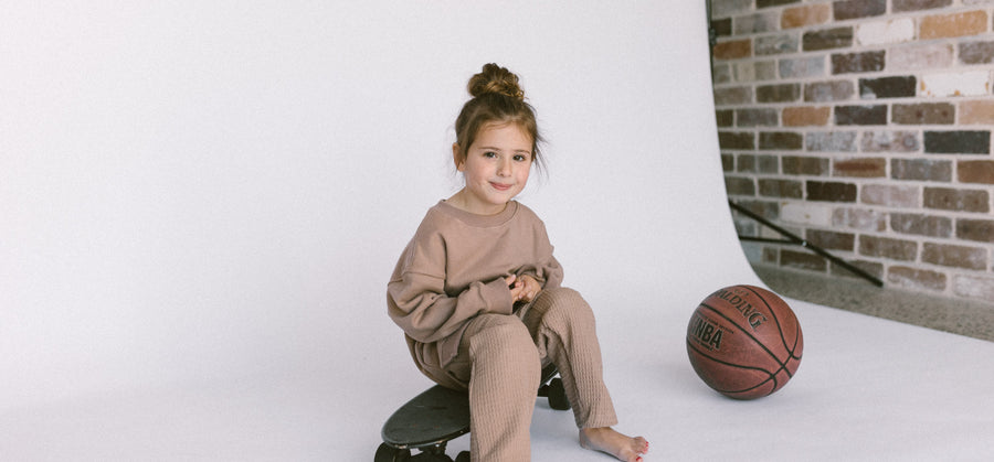 Girl sitting on a black skateboard wearing a waffle sweater set in brown by Zaja the Label